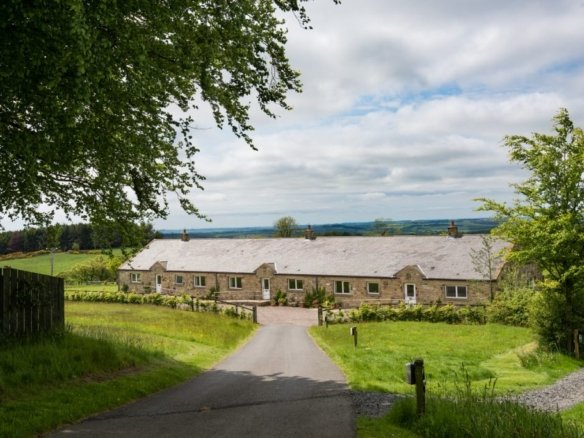 Stone cottage in lush countryside, under blue sky.