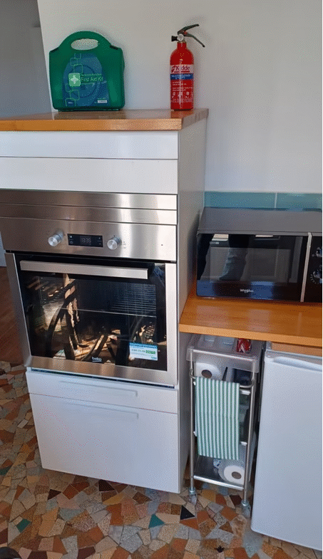 Modern kitchen with oven, microwave, fire extinguisher, first aid kit.