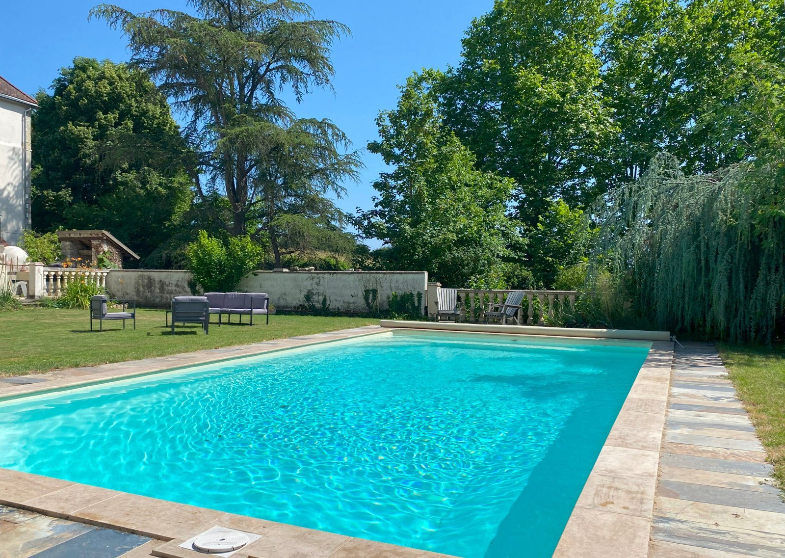 Garden swimming pool with chairs and trees.