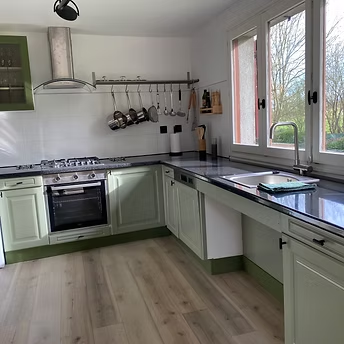 Modern kitchen with green cabinets and wooden floor.