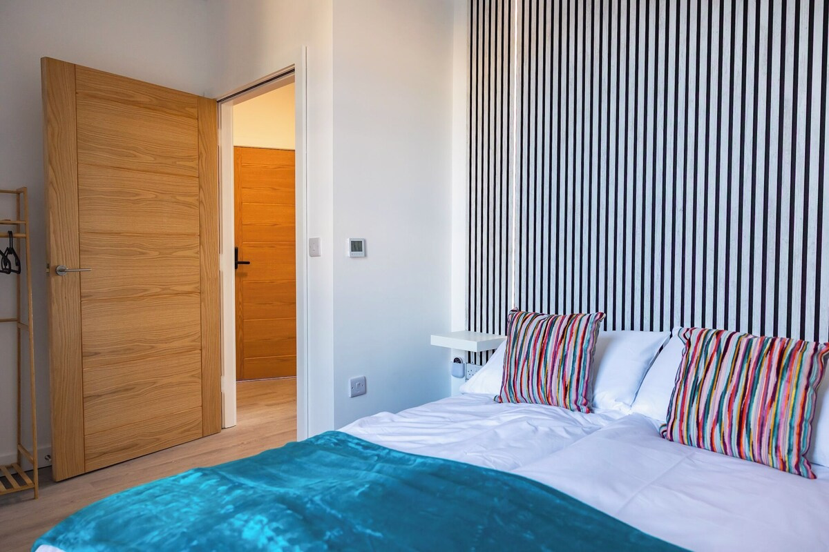 Modern bedroom with colourful pillows and striped wallpaper.