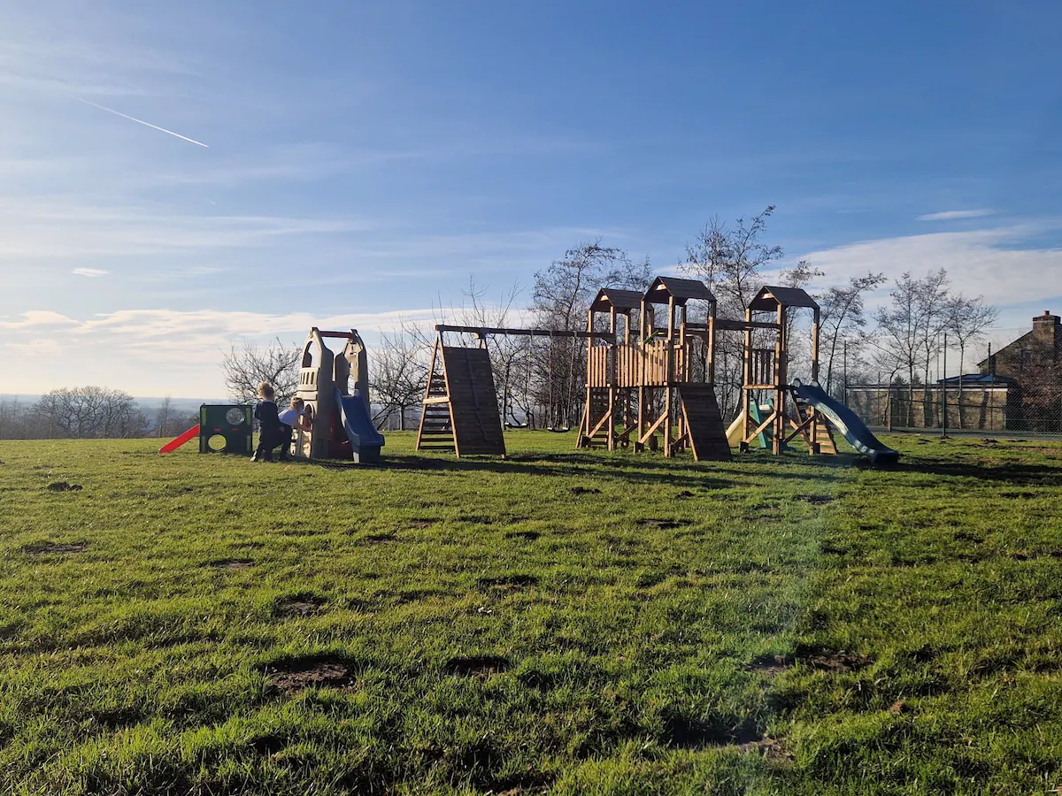 Children playing on wooden playground under blue sky.