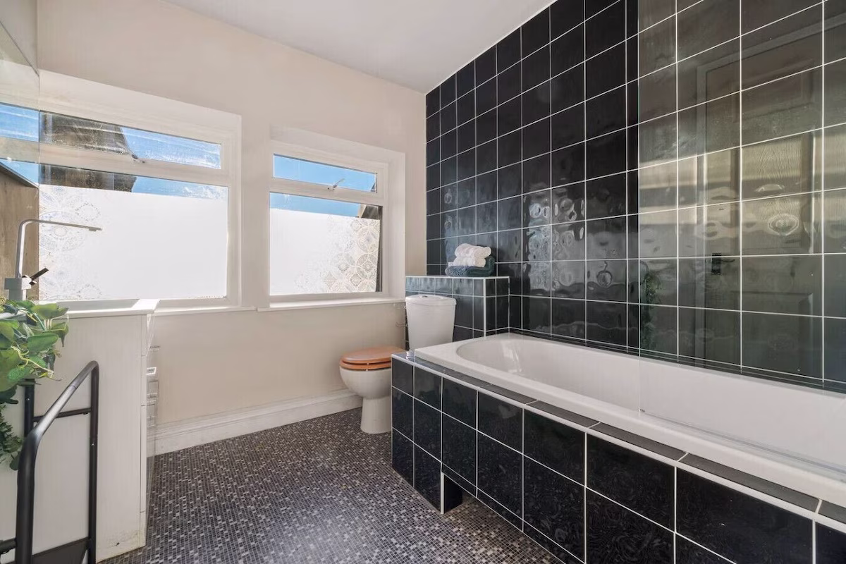 Modern bathroom with black tiled walls and bathtub.