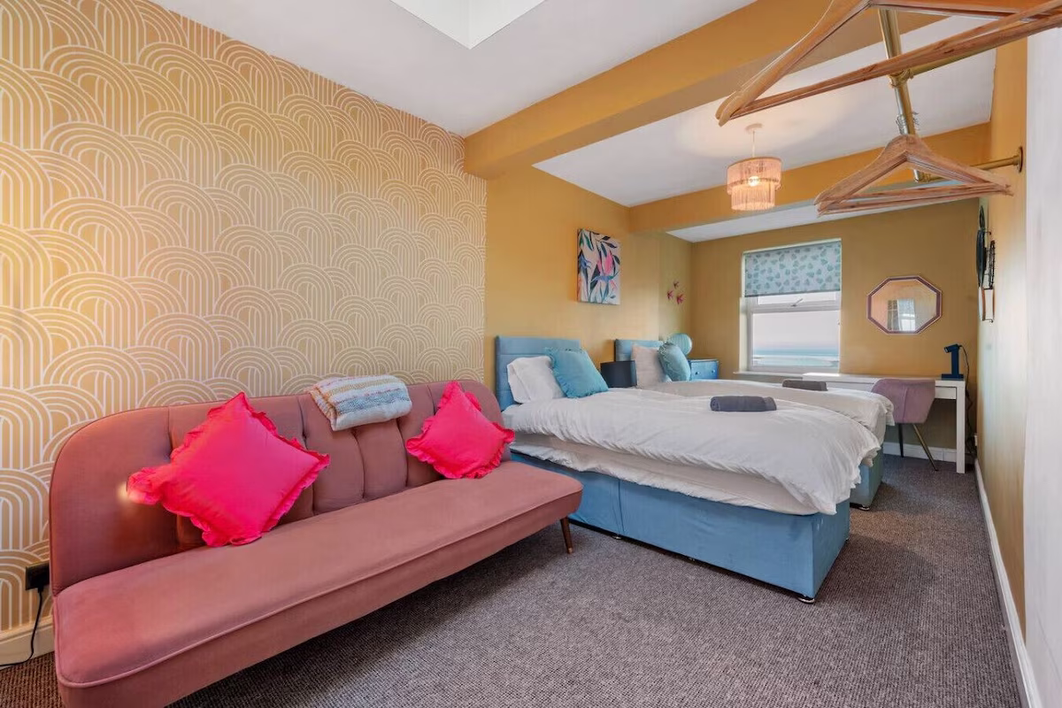 Colourful bedroom with beds, sofa, and ocean view.