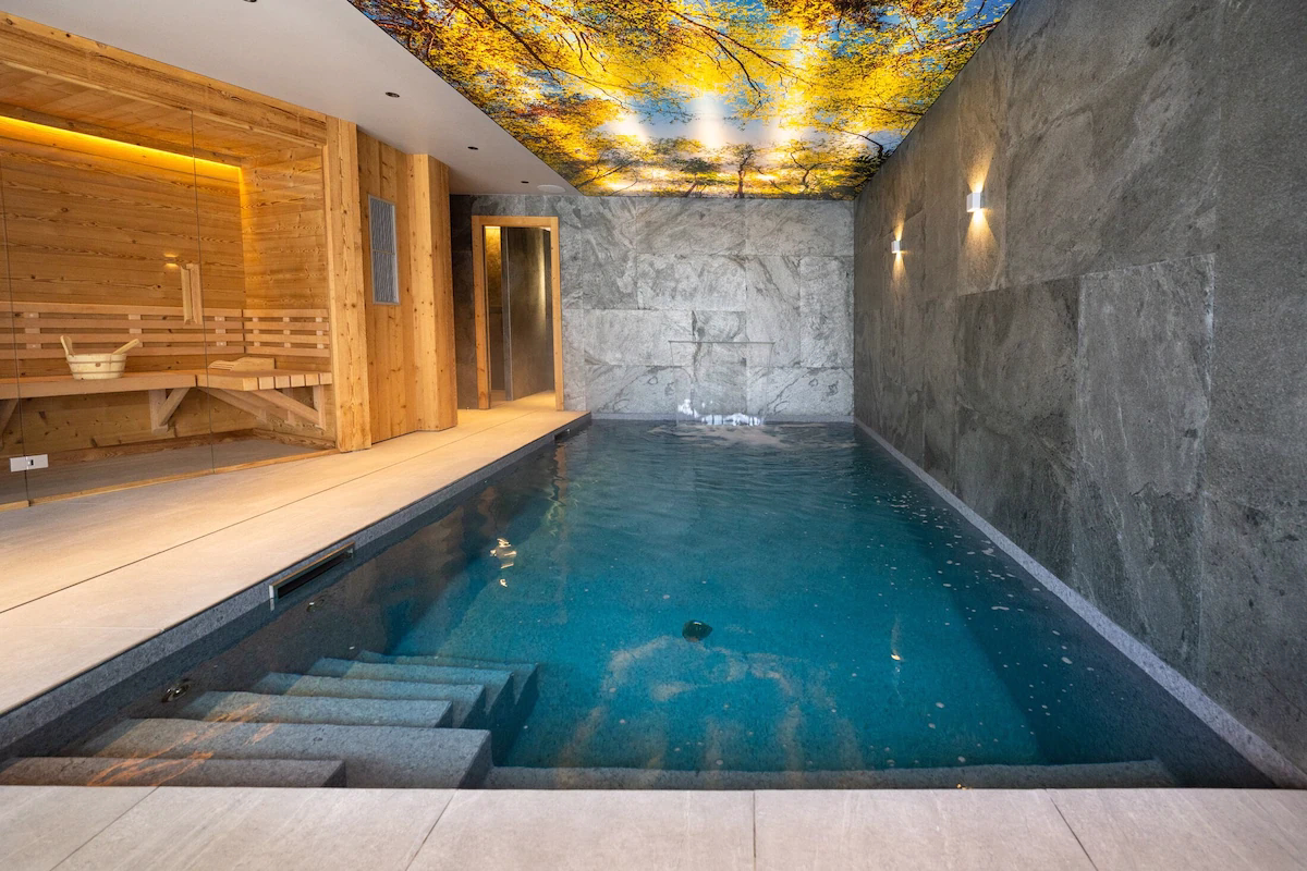 Indoor pool with wooden sauna and nature-themed ceiling.