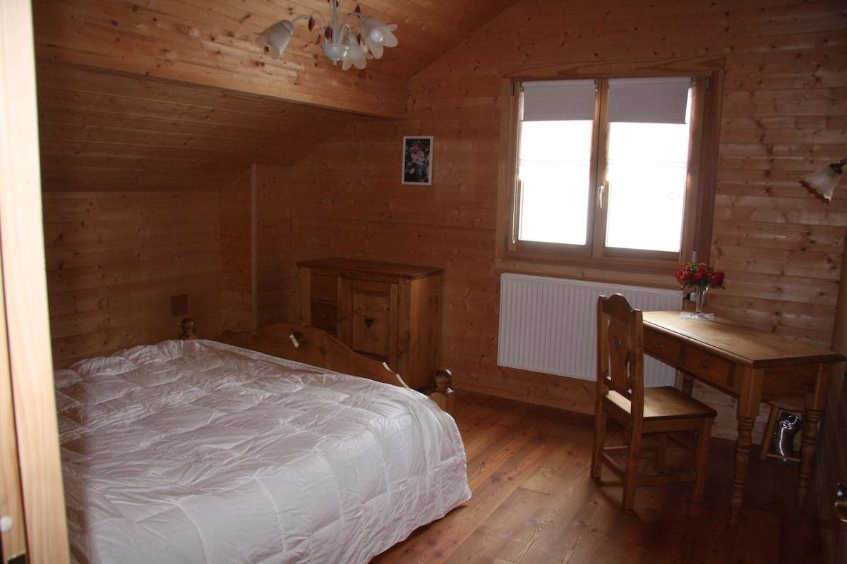 Cosy wooden cabin bedroom with desk and flowers.