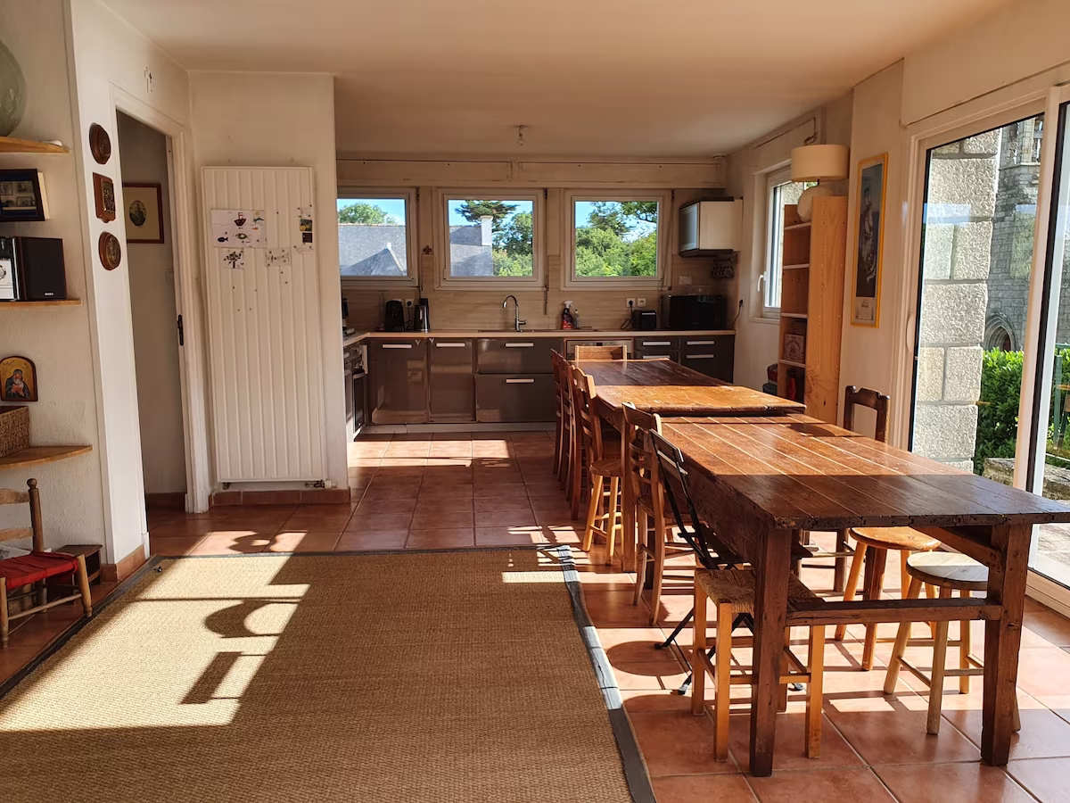 Spacious kitchen-diner with wooden tables and sunlight.