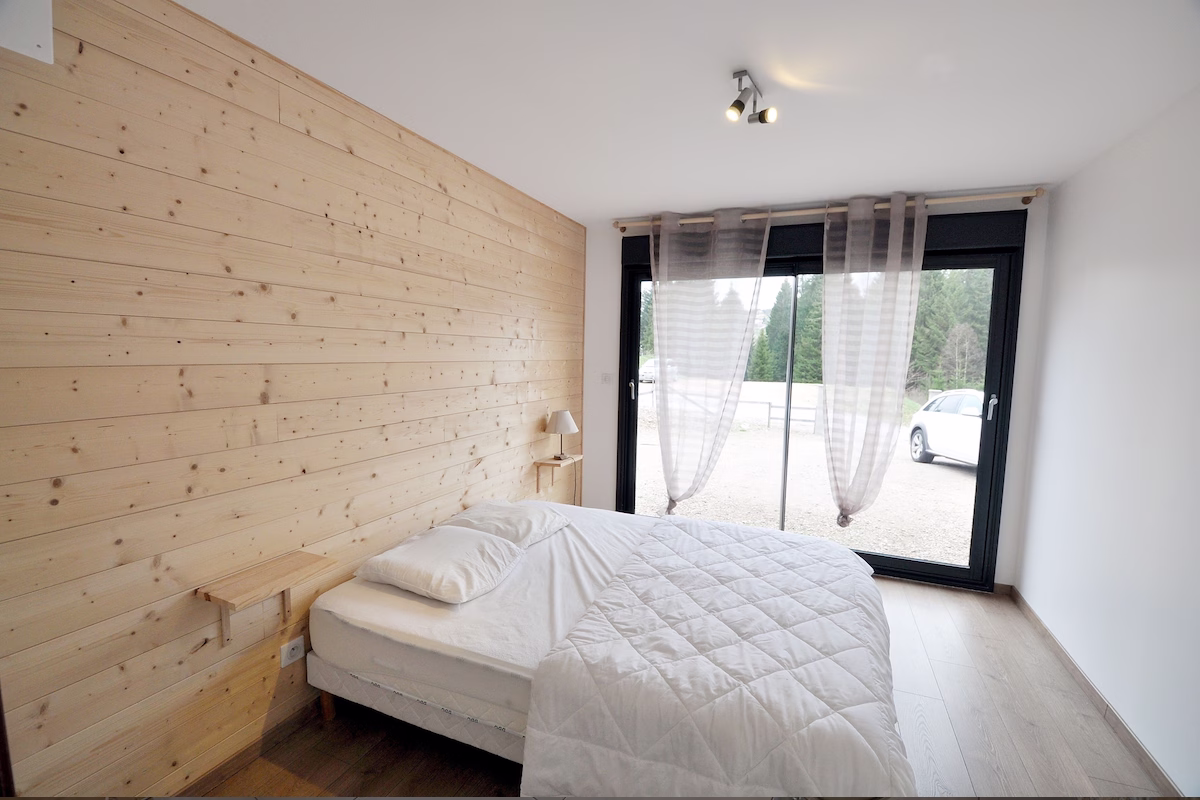 Minimalist bedroom with wooden accent wall and large window.