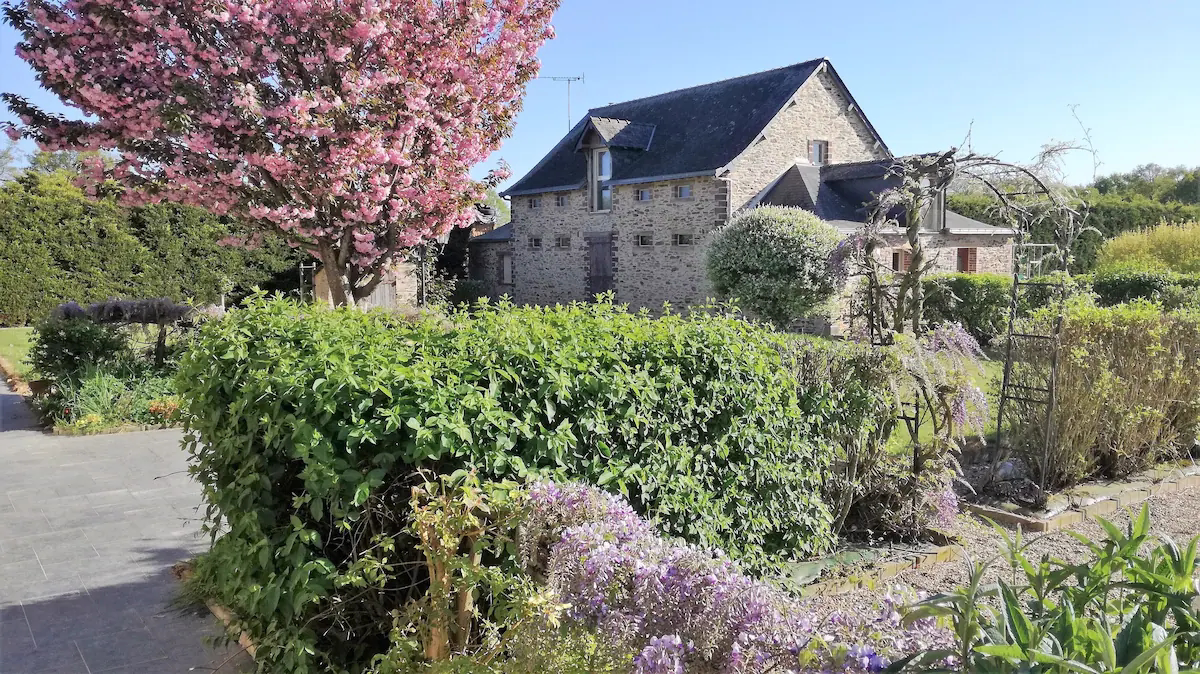 Stone cottage with garden and flowering trees.