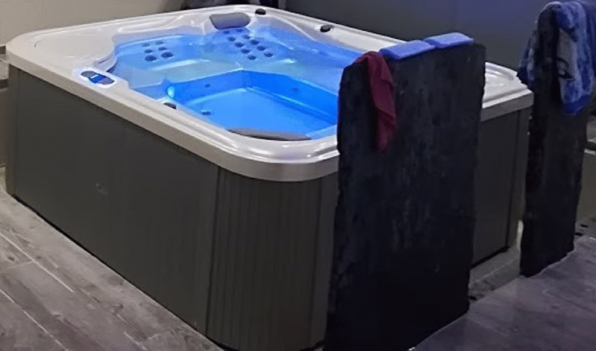 Illuminated indoor hot tub with towels on chairs.