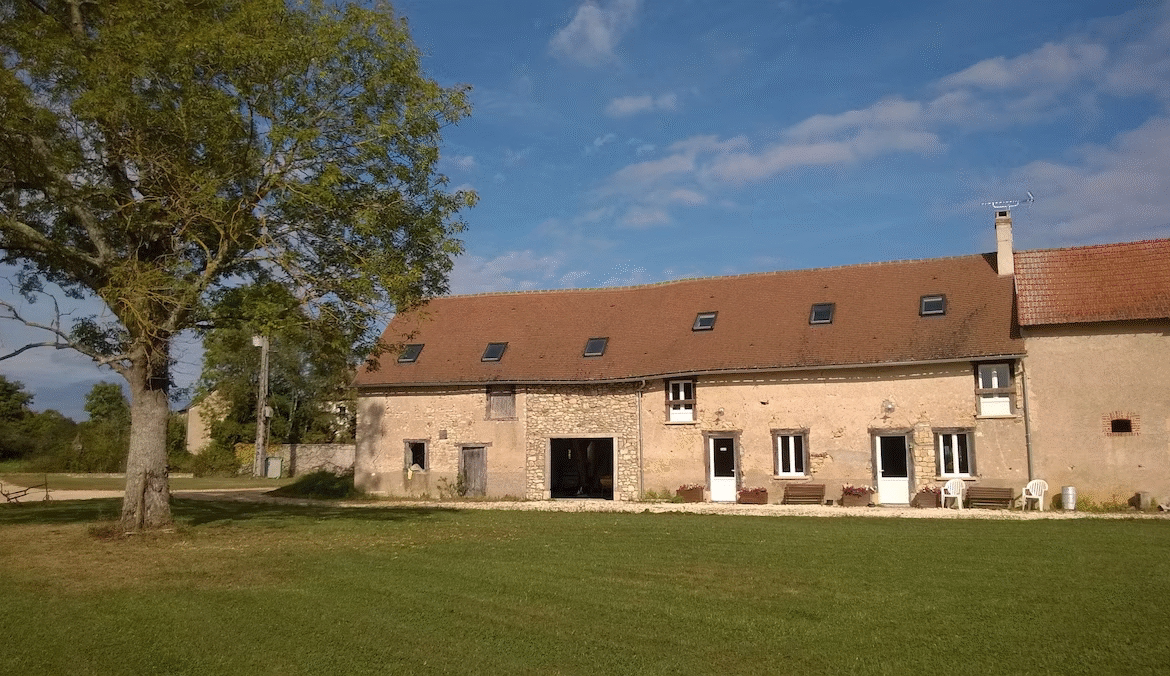 Stone farmhouse with large garden under clear sky.