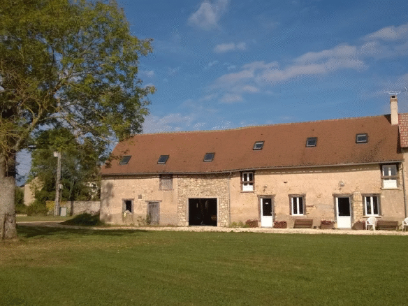Stone farmhouse with large garden under clear sky.