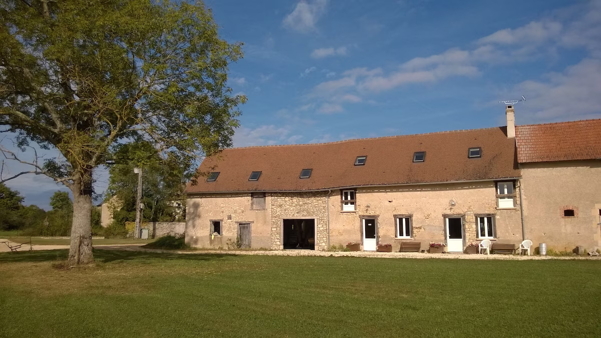 Stone farmhouse with large garden under clear sky.