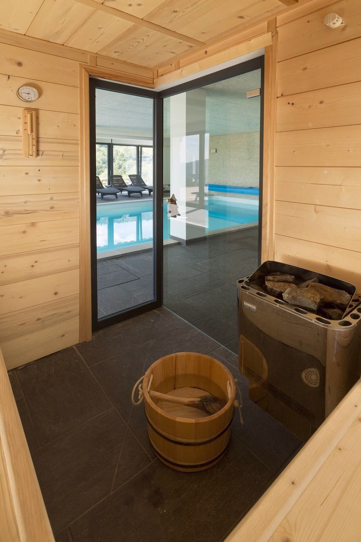 Indoor sauna with wooden bucket near swimming pool.