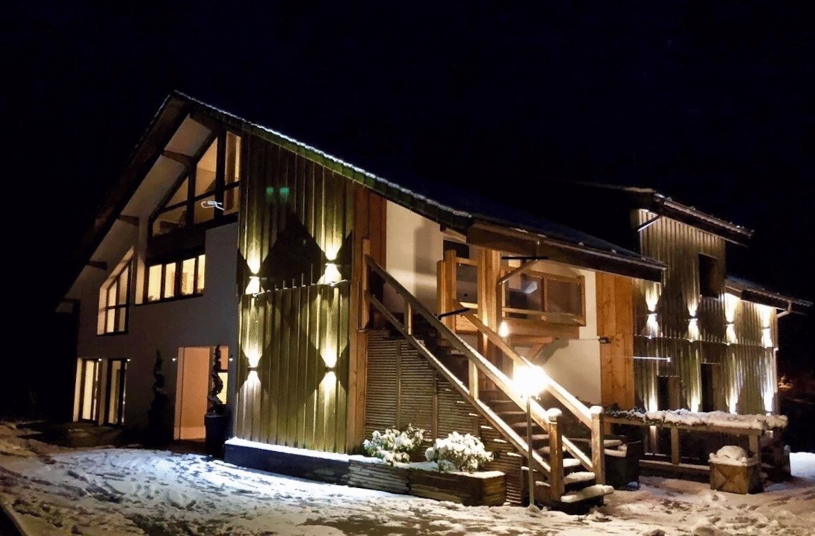 Snowy wooden house lit up at night.