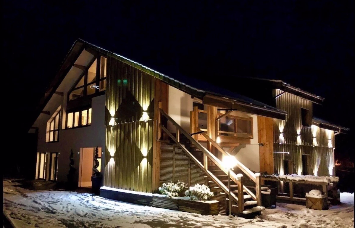 Snowy wooden house lit up at night.
