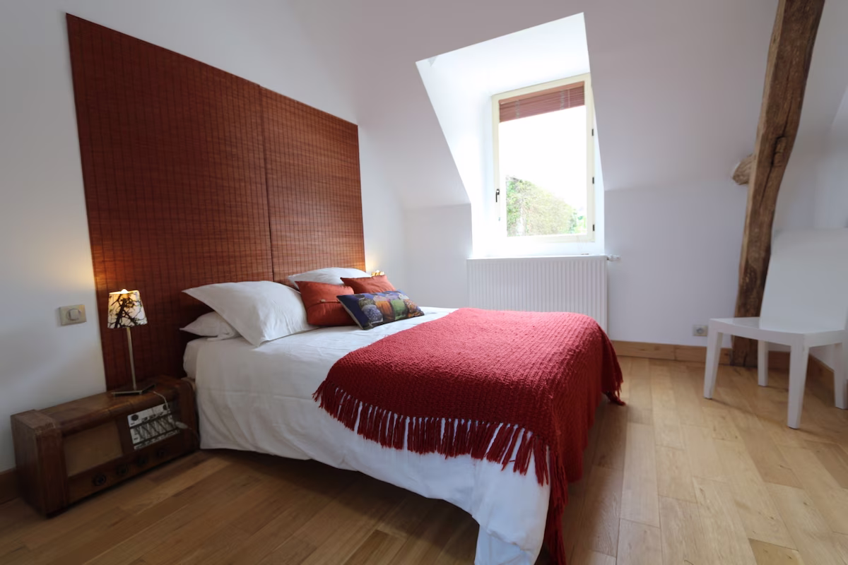 Cosy bedroom with red blanket and wooden floor.